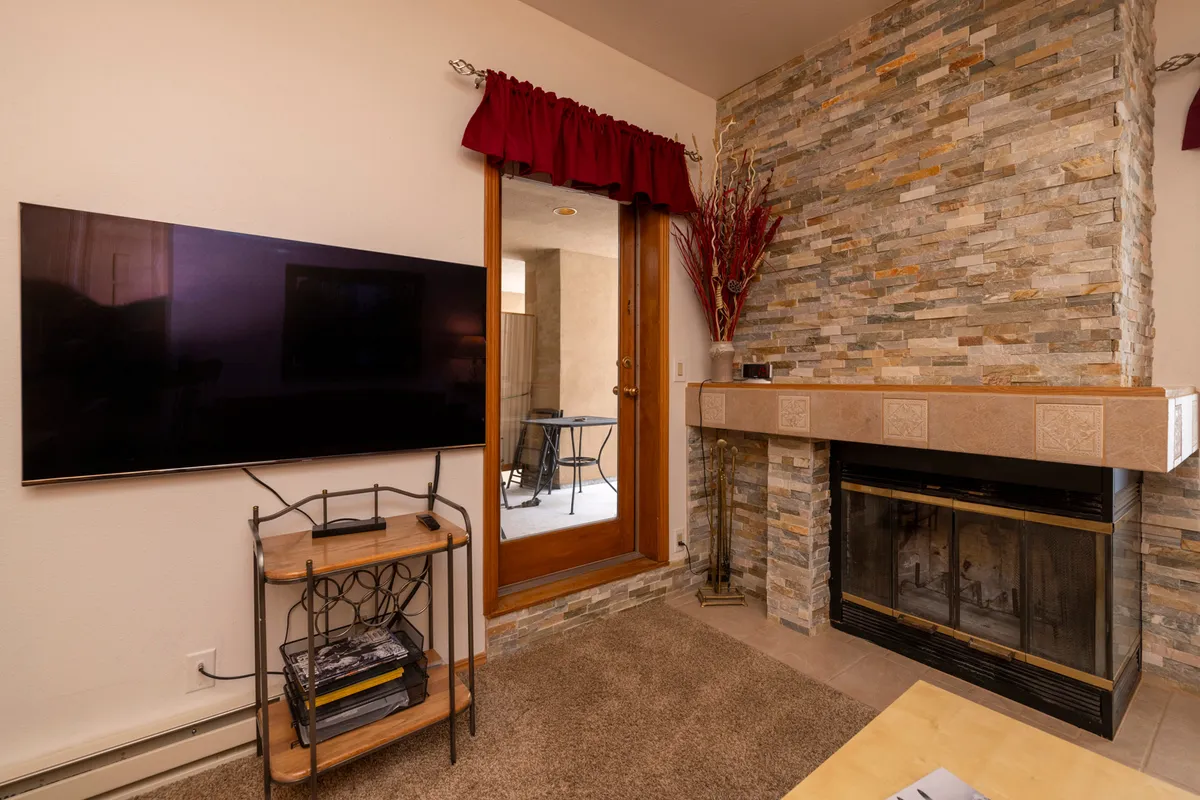 An inviting living space centered around a rustic stone fireplace, with a television, comfortable seating, and warm decorative touches. The glow of the fire enhances the sense of coziness and togetherness.