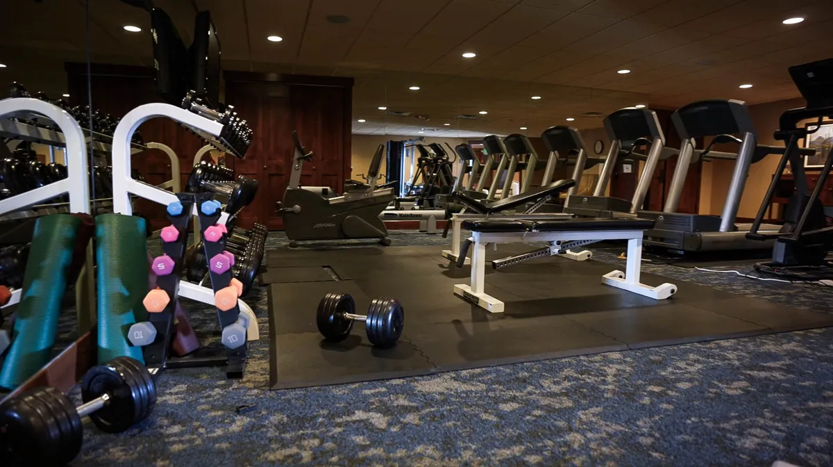 A modern fitness center with treadmills, dumbbells, a weight bench, and exercise bikes, bathed in natural light. The space is energetic, encouraging both solo workouts and social group fitness activities.