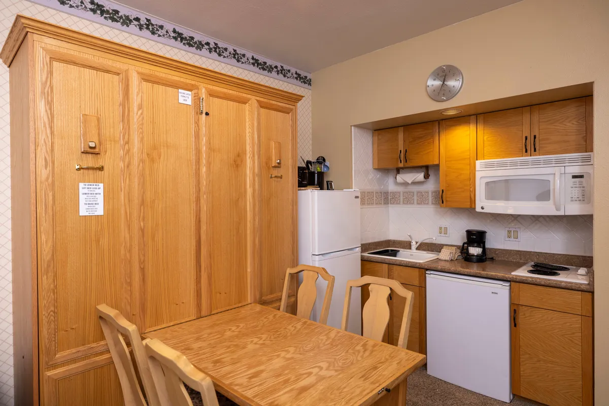 This image showcases a cozy interior space featuring wooden cabinetry, a dining table set for meals, and visible kitchen appliances. The warm lighting and inviting arrangement suggest a space designed for both cooking and socializing, with everything within easy reach.