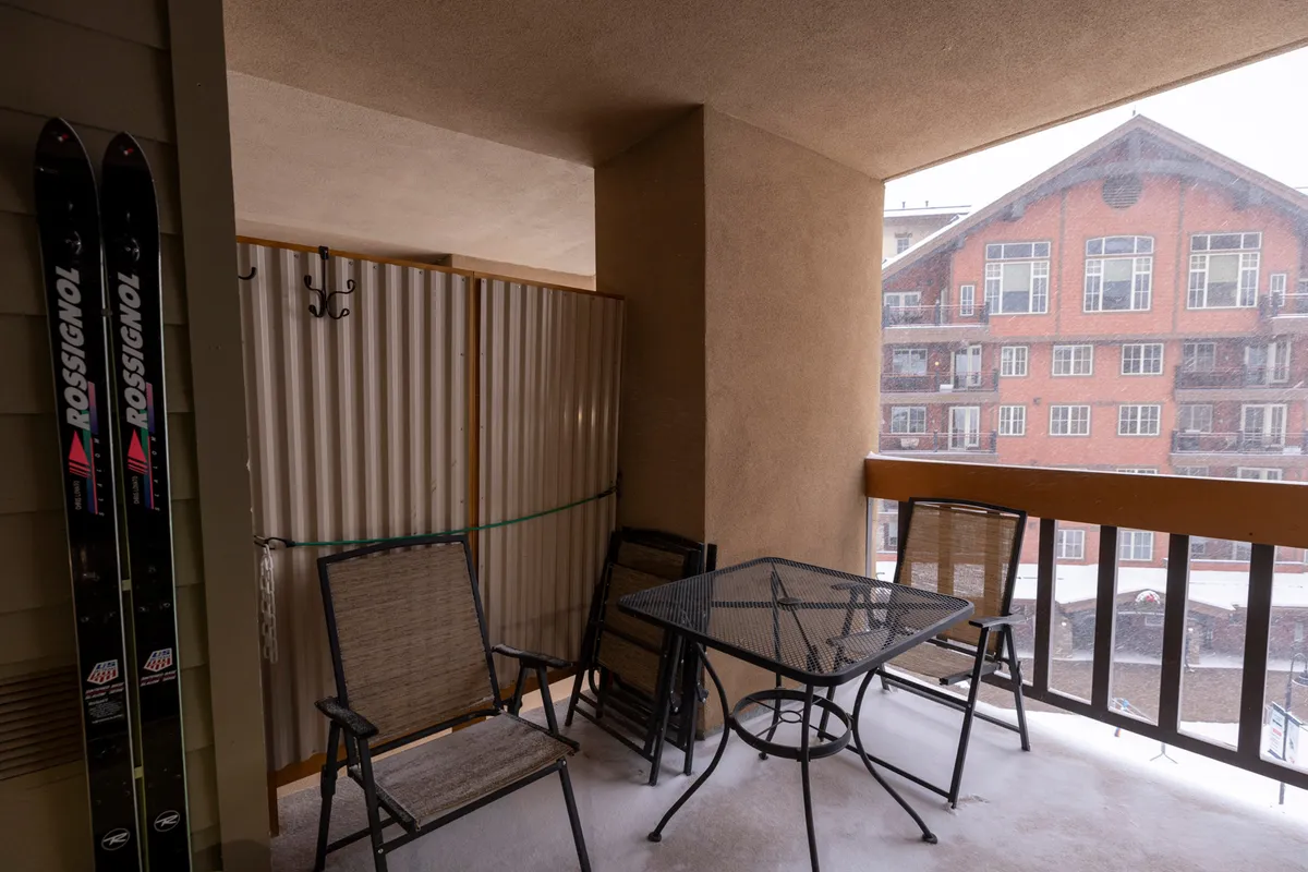 An inviting snow-covered balcony with ski equipment and outdoor seating, where someone can enjoy a hot drink after skiing. The scene radiates comfort and relaxation after a day of slopeside adventure.